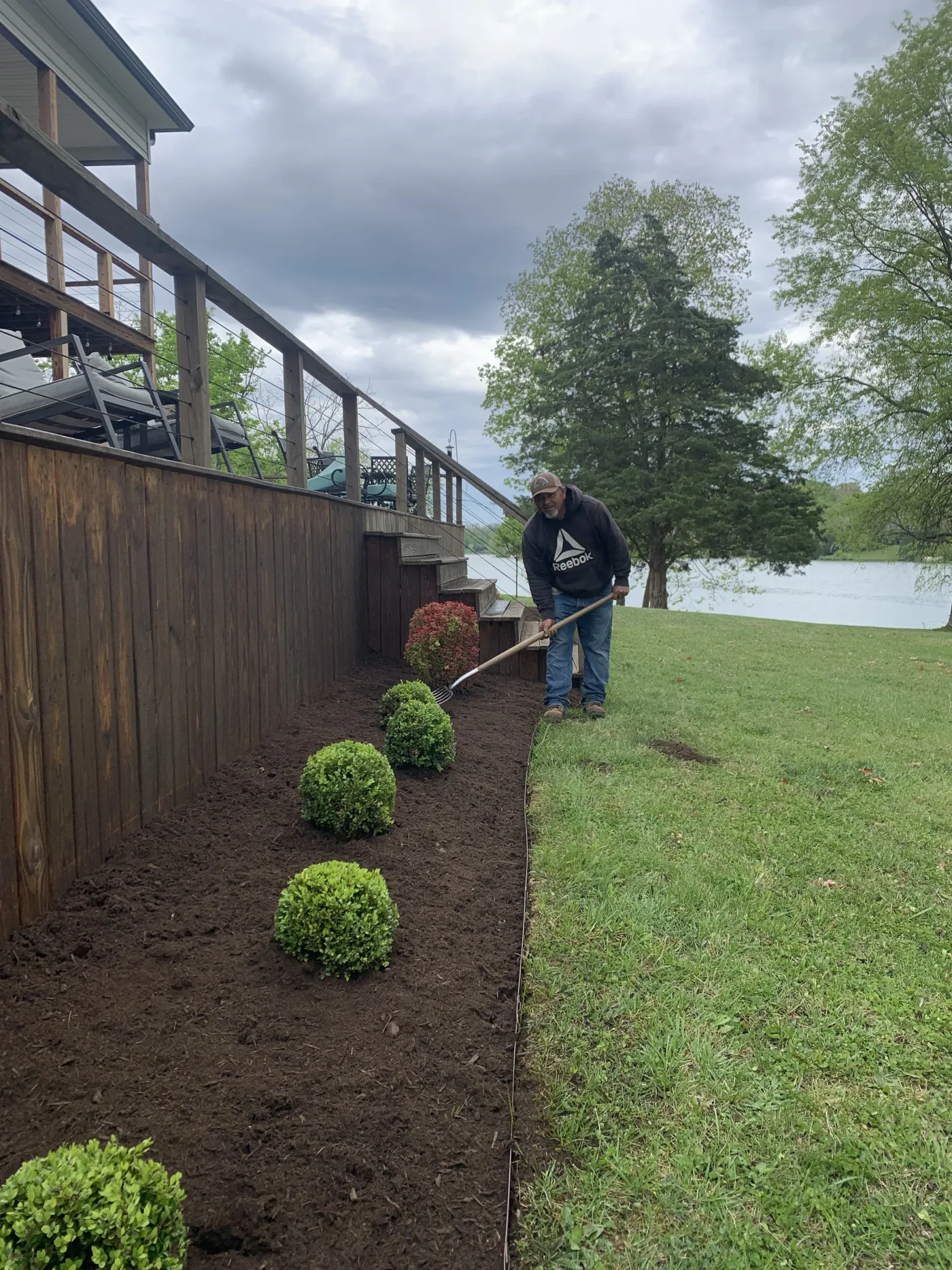 Crew installing boxwood shrubs along a residential deck with fresh mulch